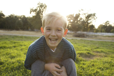 Boy holding his little brother down and looks at the camera and smiles. - AURF01284