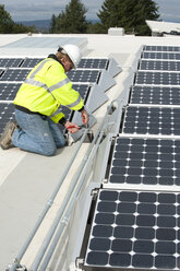 Green energy technician adjusts photovoltaic panels on a roof - AURF01328