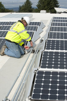 Techniker für grüne Energie justiert Fotovoltaikmodule auf einem Dach - AURF01328