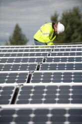 Techniker für grüne Energie justiert Fotovoltaikmodule auf einem Dach - AURF01329