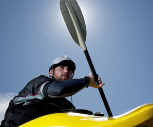 Tiefblick auf einen männlichen Kajakfahrer in einem Spielboot im Gegenlicht der Sonne. - AURF01359