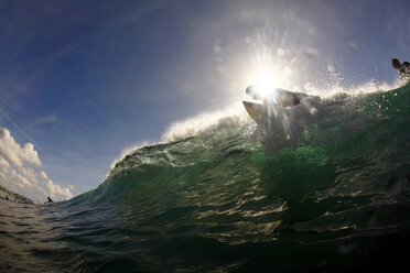 Low-angle view of a surfer on top of a green wave, backlit by the sun. - AURF01360