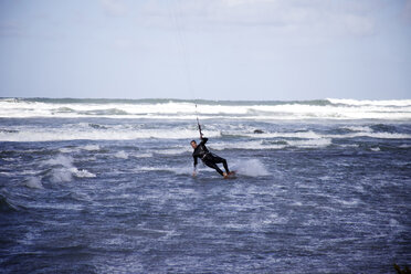 Ein männlicher Kitesurfer ändert die Richtung und berührt das Wasser, während er sich dreht. - AURF01361