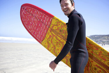 Ein männlicher Surfer läuft lächelnd auf das Wasser zu. - AURF01362