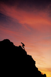 Mann klettert bei Sonnenuntergang auf einen Grat. - AURF01372