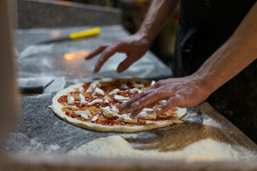 Nahaufnahme eines Pizzabäckers bei der Zubereitung einer Pizza mit Tomatensauce und Mozzarella in der Küche - AFVF01433