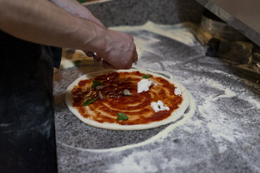 Nahaufnahme eines Pizzabäckers bei der Zubereitung einer Pizza mit Tomatensauce und Mozzarella in der Küche - AFVF01439