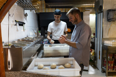 Zwei Männer mit rohem Teig in Kisten in der Küche einer Pizzeria - AFVF01456