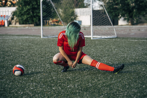 Junge Frau dehnt sich auf dem Fußballplatz neben dem Ball - VPIF00507