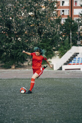 Junge Frau spielt Fußball auf einem Fußballplatz und schießt den Ball - VPIF00510