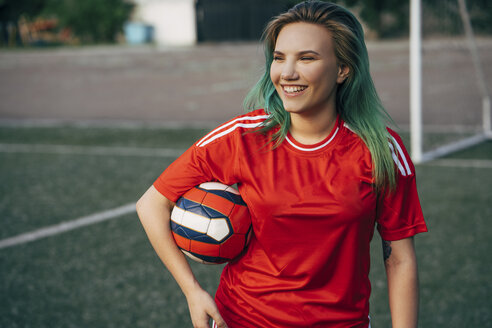 Lächelnde junge Frau steht auf dem Fußballplatz und hält den Ball - VPIF00513