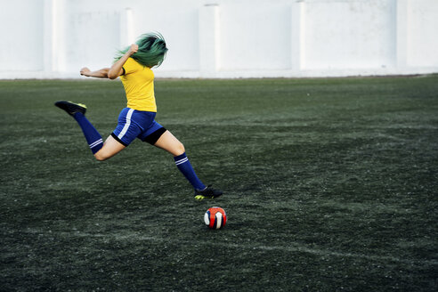 Junge Frau spielt Fußball auf einem Fußballplatz und schießt den Ball - VPIF00517