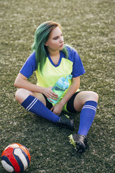 Junge Frau sitzt mit Wasserflasche und Ball auf dem Fußballplatz - VPIF00520