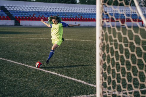 Junge Frau spielt Fußball auf einem Fußballplatz und schießt den Ball - VPIF00521
