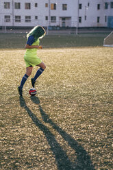 Junge Frau spielt Fußball auf einem Fußballplatz und dribbelt mit dem Ball - VPIF00524