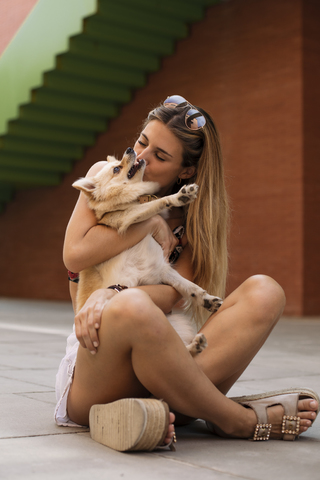 Lächelnde junge Frau sitzt und küsst ihren Hund, lizenzfreies Stockfoto