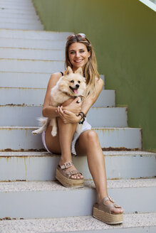 Smiling young woman sitting on stairs holding her dog - ACPF00256