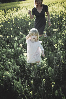 Porträt eines kleinen Mädchens, das mit seiner Mutter auf einem Rapsfeld spazieren geht - PSIF00018