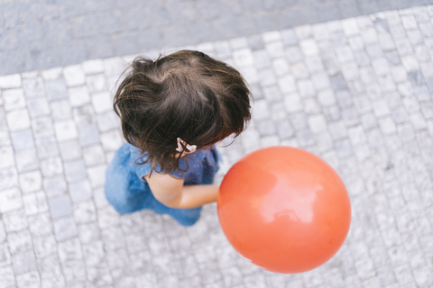 Baby-Mädchen mit rotem Luftballon auf dem Bürgersteig, Ansicht von oben, lizenzfreies Stockfoto