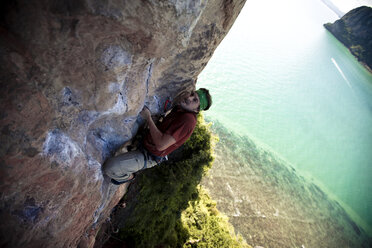 Strained male climber looks to his next move on a limestone beach cliff in Thailand. - AURF01399