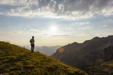 Germany, Bavaria, Oberstdorf, man on a hike in the mountains looking at view at sunset - DIGF04983