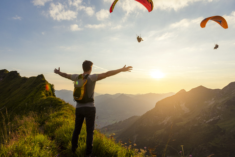 Deutschland, Bayern, Oberstdorf, Mann auf einer Wanderung in den Bergen bei Sonnenuntergang mit Paraglider im Hintergrund, lizenzfreies Stockfoto