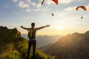 Deutschland, Bayern, Oberstdorf, Mann auf einer Wanderung in den Bergen bei Sonnenuntergang mit Paraglider im Hintergrund - DIGF04989