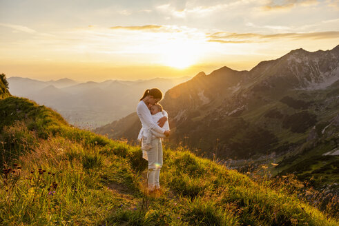 Germany, Bavaria, Oberstdorf, mother holding little daughter on a hike in the mountains at sunset - DIGF04993