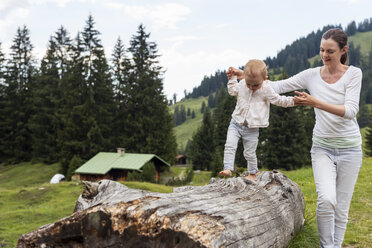 Deutschland, Bayern, Oberstdorf, Mutter hilft kleiner Tochter beim Balancieren auf einem Baumstamm - DIGF05005