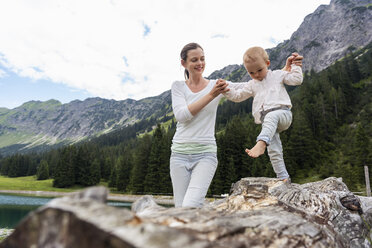 Germany, Bavaria, Oberstdorf, mother helping little daughter balancing on a log - DIGF05006