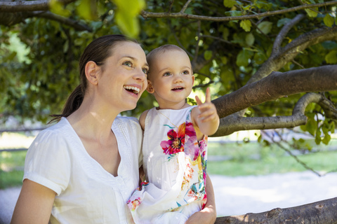 Glückliche Mutter und kleine Tochter unter einem Baum, die etwas entdecken, lizenzfreies Stockfoto