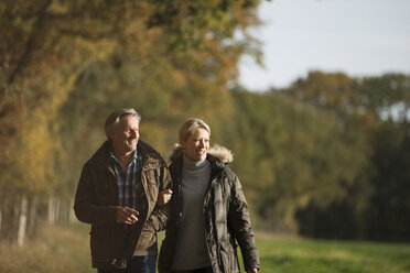Älteres Paar, das Arm in Arm in einem sonnigen Herbstpark spazieren geht - HOXF03675