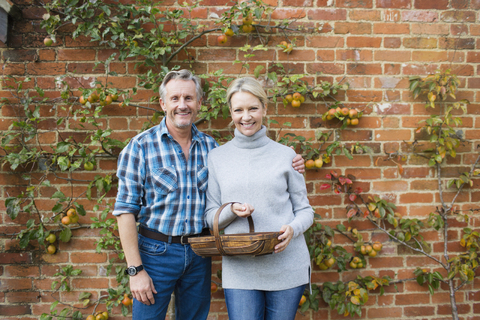 Porträt lächelndes reifes Paar beim Ernten von Äpfeln im Garten, lizenzfreies Stockfoto