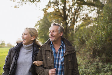 Happy mature couple walking arm in arm in autumn park - HOXF03706