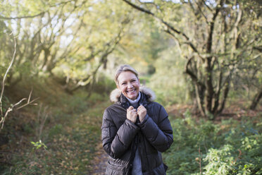 Portrait confident mature woman in parka in sunny autumn woods - HOXF03721