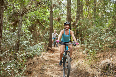 Carefree woman mountain biking on trail in woods - CAIF21318