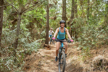 Unbekümmerte Frau beim Mountainbiken auf einem Waldweg - CAIF21318