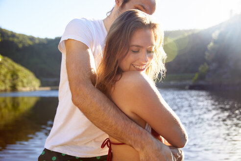Zärtliches Paar, das sich am sonnigen Sommersee umarmt - CAIF21327
