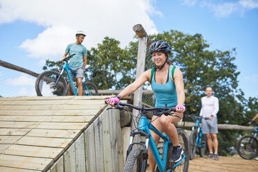 Smiling young woman mountain biking at obstacle course - CAIF21343