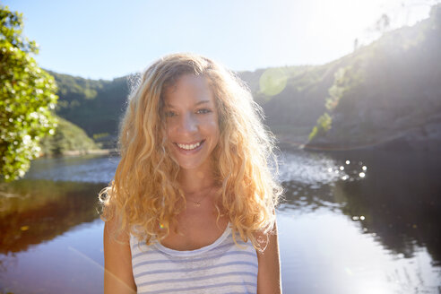 Porträt lächelnde, selbstbewusste junge Frau am sonnigen Sommersee - CAIF21346