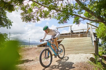 Konzentrierter Mann fährt mit dem Mountainbike eine sonnige Hindernisbahn-Rampe hinunter - CAIF21355