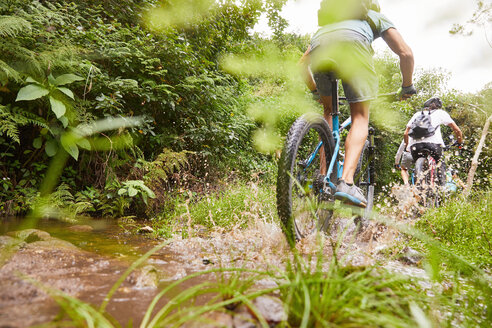 Man mountain biking, splashing on muddy trail - CAIF21360