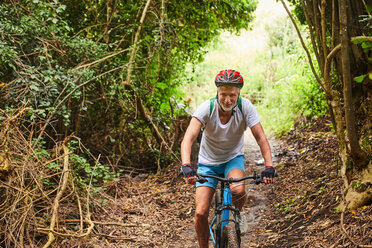 Älterer Mann beim Mountainbiken auf einem Pfad im Wald - CAIF21369