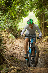Glücklicher Mann beim Mountainbiken auf einem Waldweg - CAIF21371
