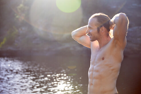 Unbeschwerter Mann mit nacktem Oberkörper am sonnigen Sommersee - CAIF21374