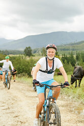 Lächelnder, selbstbewusster reifer Mann beim Mountainbiking auf einem ländlichen Feldweg - CAIF21378