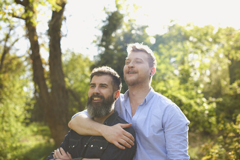 Zärtliches männliches schwules Paar, das sich im sonnigen Park umarmt - CAIF21380