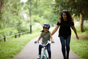 Glückliche Mutter bringt ihrer Tochter das Fahrradfahren bei - CAIF21388
