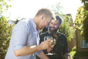 Glückliches männliches schwules Paar trinkt Wein im sonnigen Garten - CAIF21393