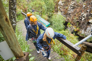 Friends walking on bridge, preparing to zip line - CAIF21436